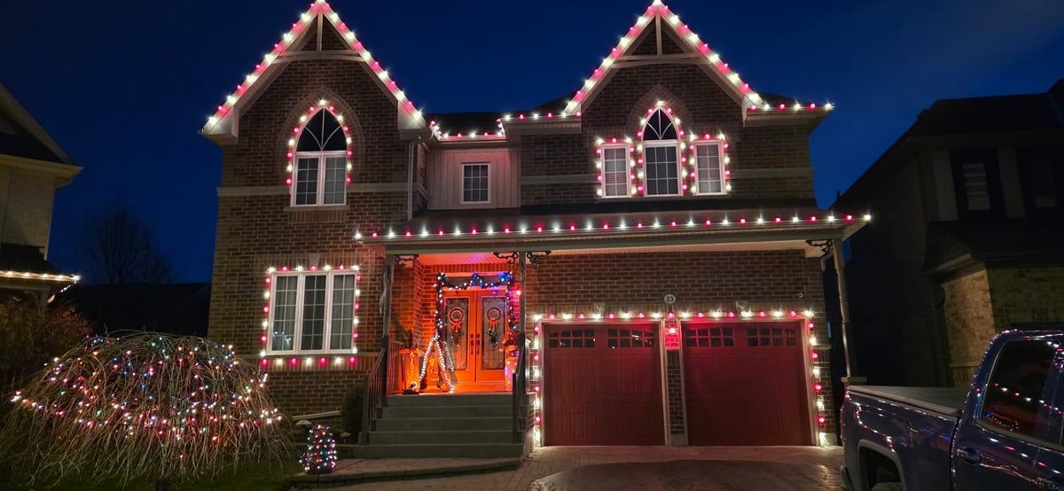 Brick house decorated with extensive holiday lights and red festive banner on garage at dusk