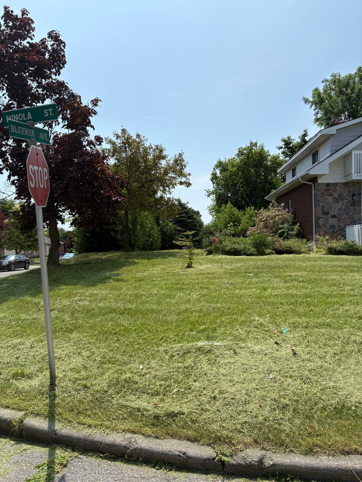Street corner with STOP sign, large green lawn, mature trees, and brick house on sunny day