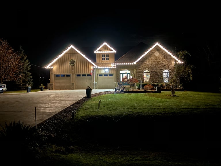 Large brick and stone home illuminated at night with decorative landscape lighting along roofline and stone driveway.