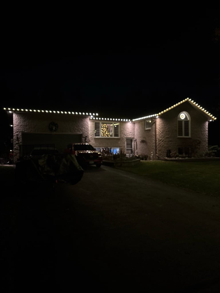 Brick house at night decorated with warm white string lights outlining the roofline and architectural features