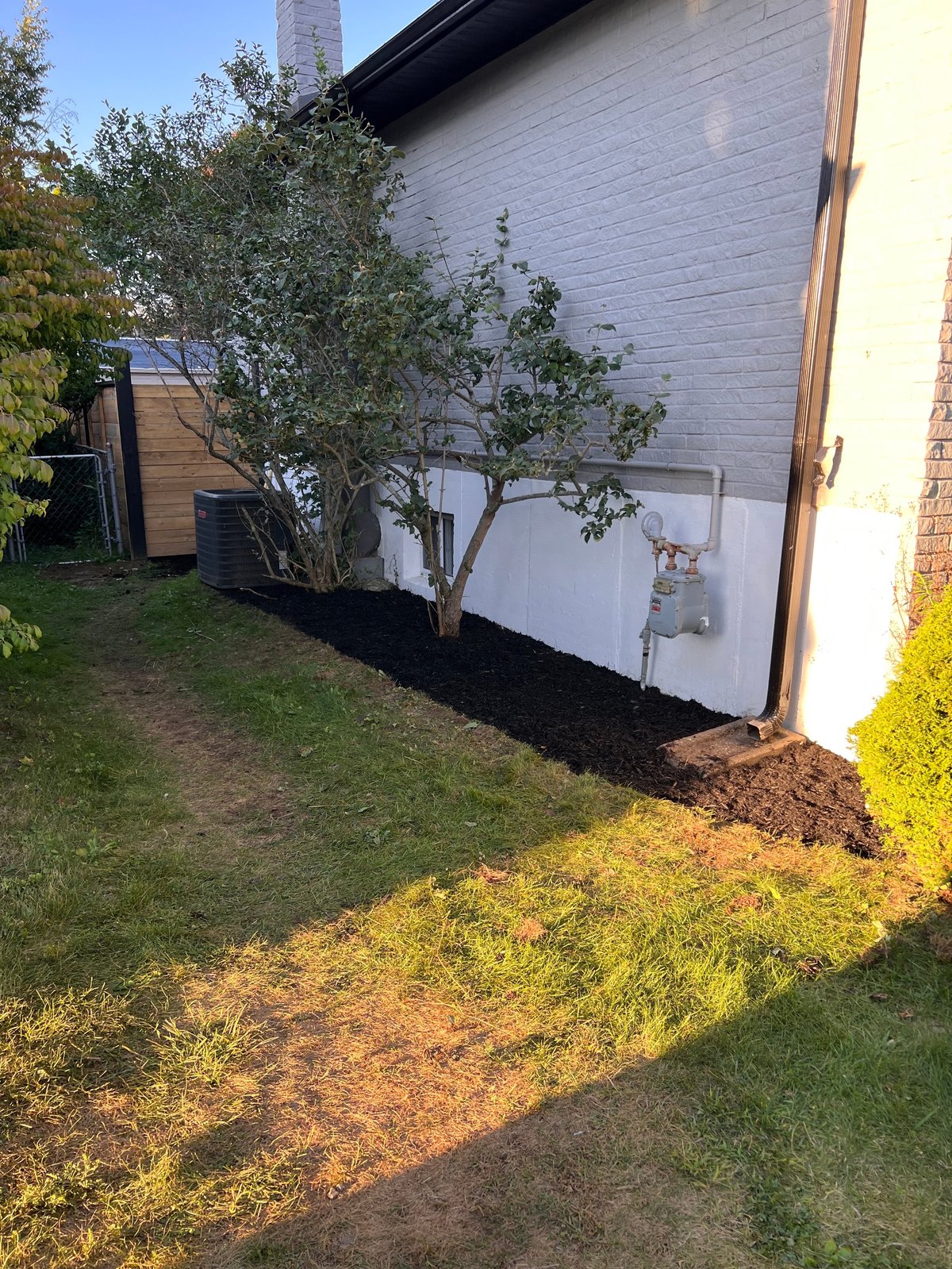 White outdoor storage shed against brick wall with young tree and landscaping in yard