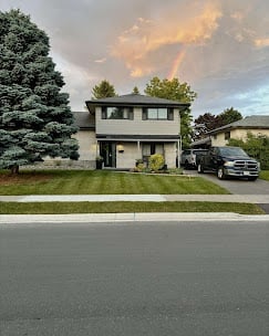 Two-story modern house with black exterior, parked truck in driveway, green landscaping, and cloudy sky at dusk